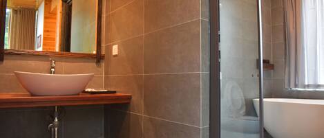 A modern bathroom with a large vessel sink, a freestanding bathtub, and a glass-enclosed shower.