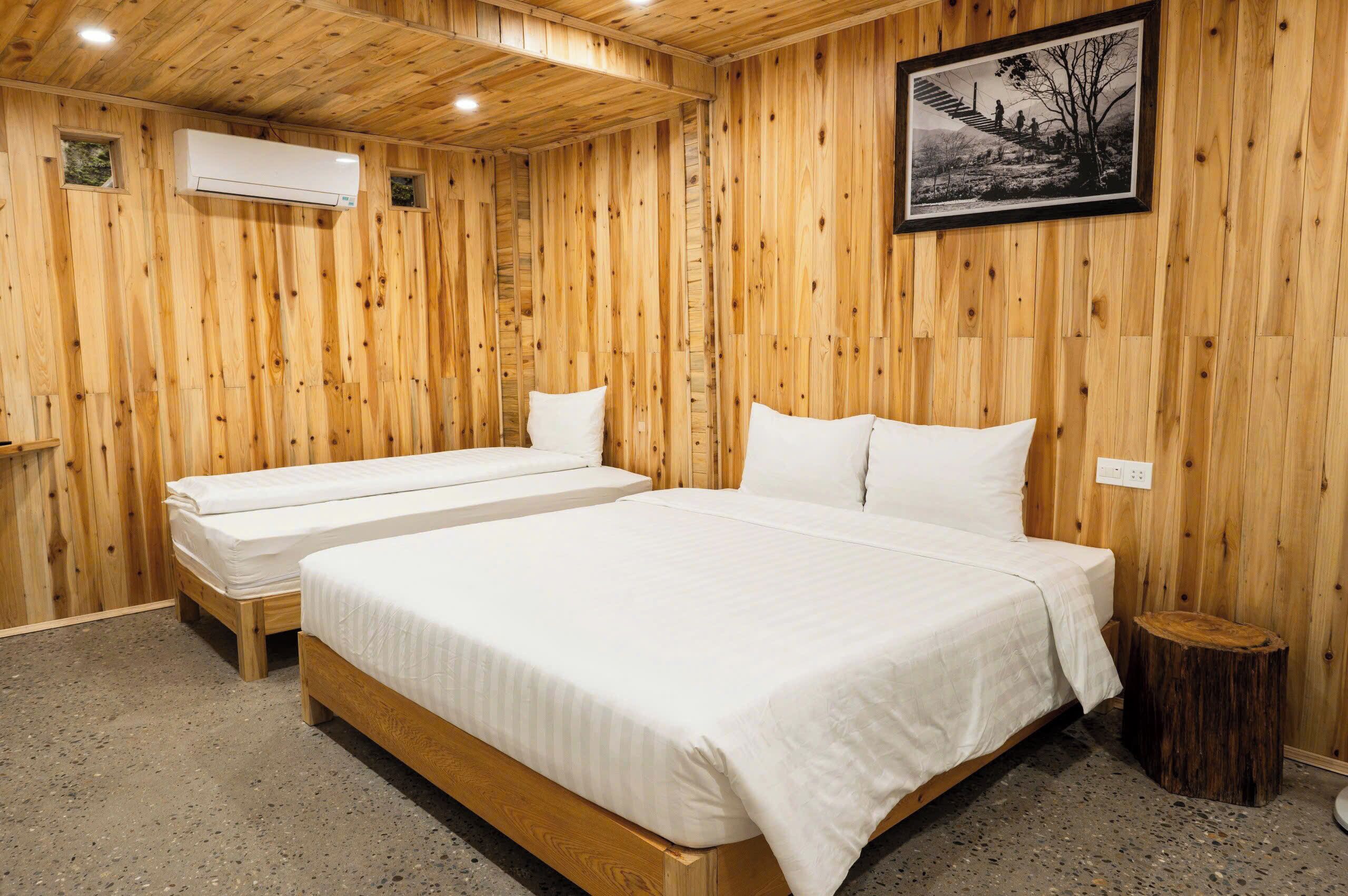 Een kamer met houten lambrisering, twee bedden, een airconditioning en een lijst met een foto, plus een klein houten krukje.
