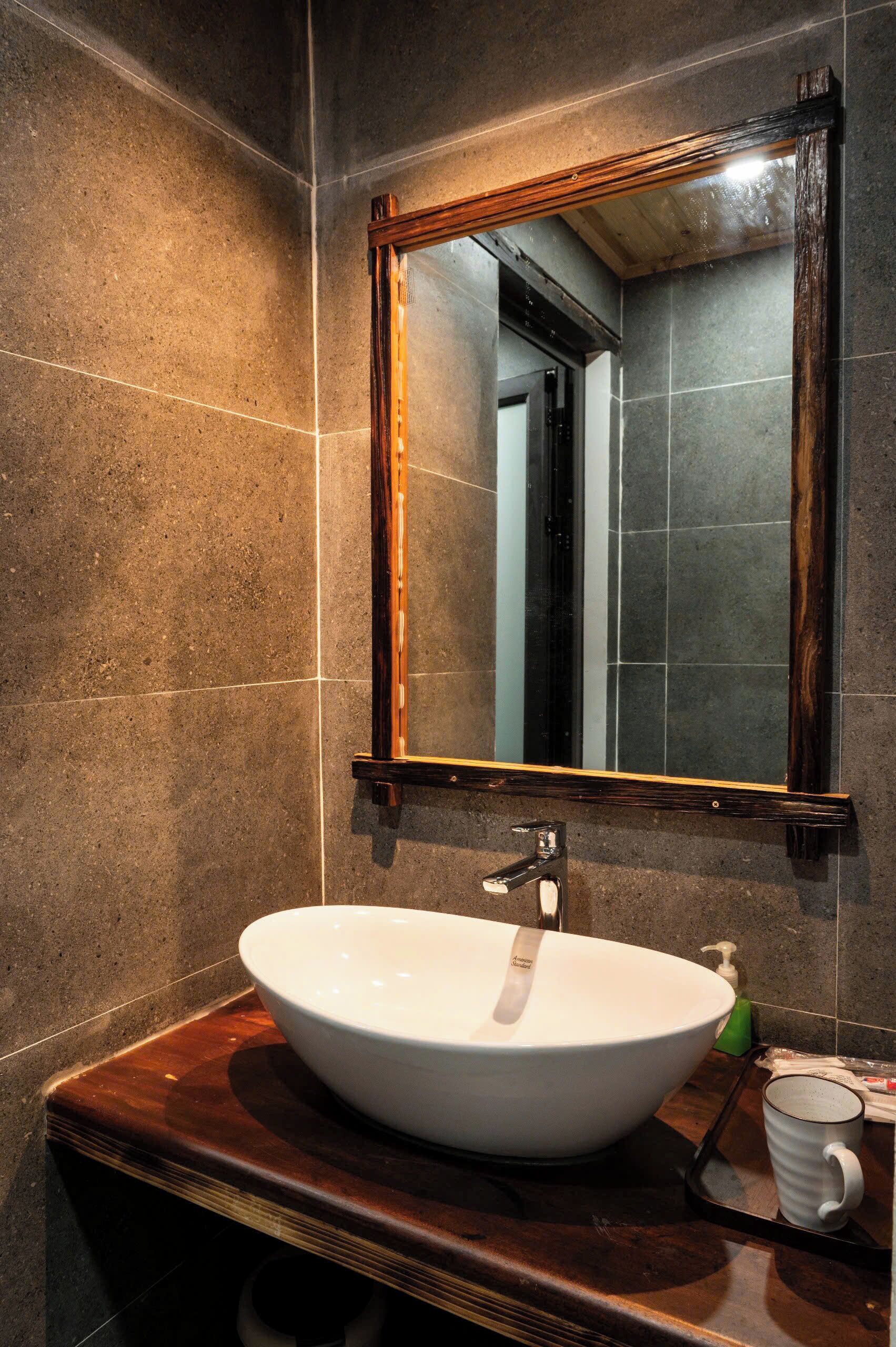 A bathroom with a large white sink, a wooden-framed mirror, and a dark brown countertop.