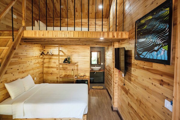 L'intérieur d'une cabane en bois, avec un lit, un lavabo et un tableau.