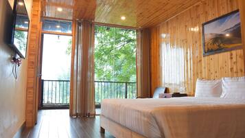 A wooden-paneled bedroom with a large bed, a painting, and a view of trees through a window.