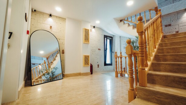 Um interior amplo com escadaria de madeira, um espelho grande refletindo a escada, e uma parede de tijolos.