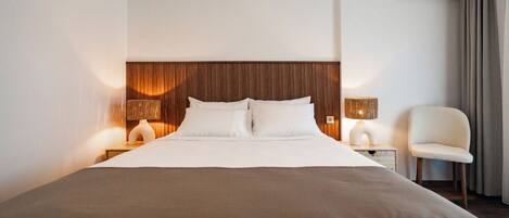 A hotel room with a large bed, two bedside lamps, a chair, and an air conditioning unit.