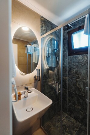 A modern bathroom with a glass-enclosed shower, a sink with a mirror, and a window providing natural light. - Rodones 1924 (Urla)