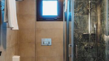 A bathroom with a toilet, a trash can, a towel rack, a window, and a glass-enclosed shower.