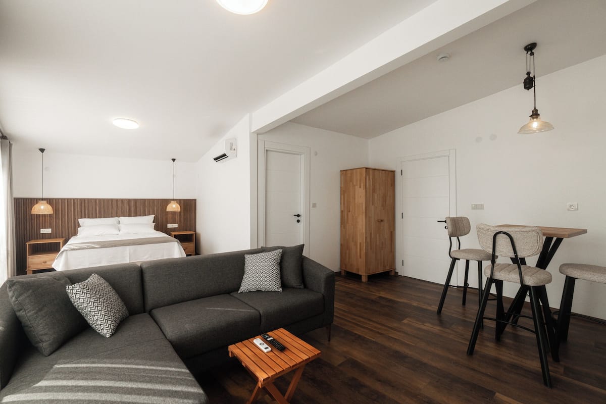 A modern room with a sofa, a wooden cabinet, a dining table with chairs, and a bed with a wooden headboard.