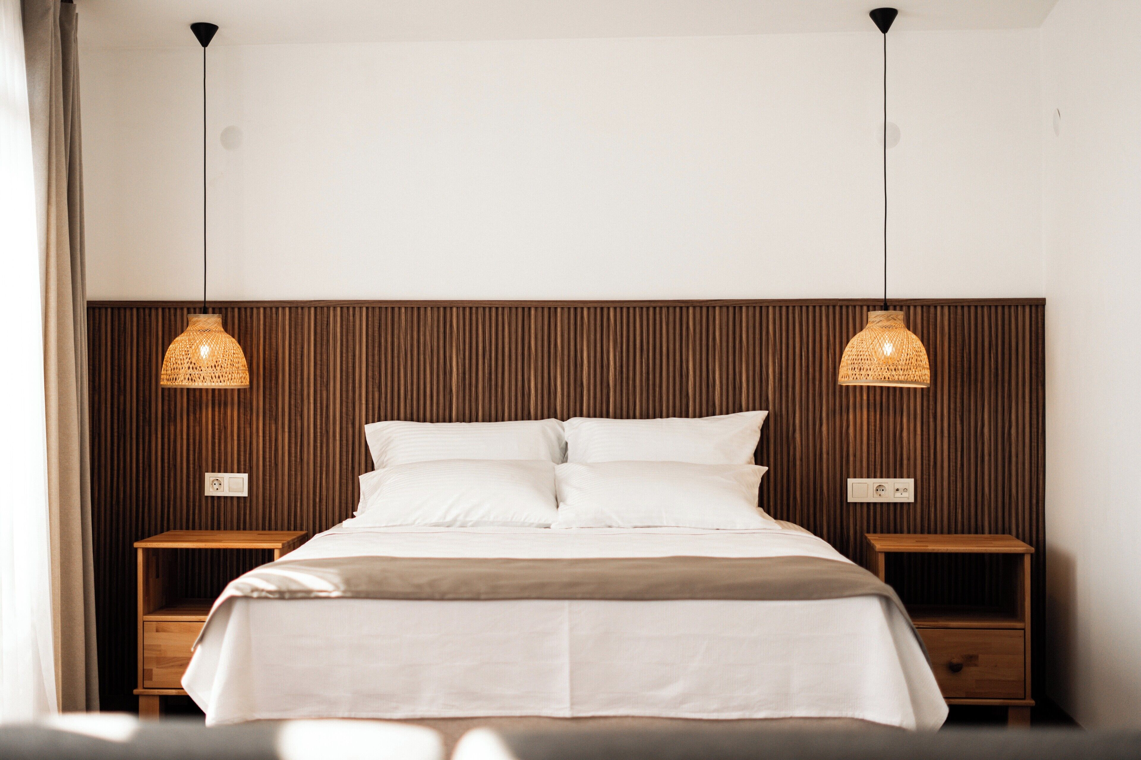 A neatly made bed with a wooden headboard, two bedside tables, and two hanging lamps.