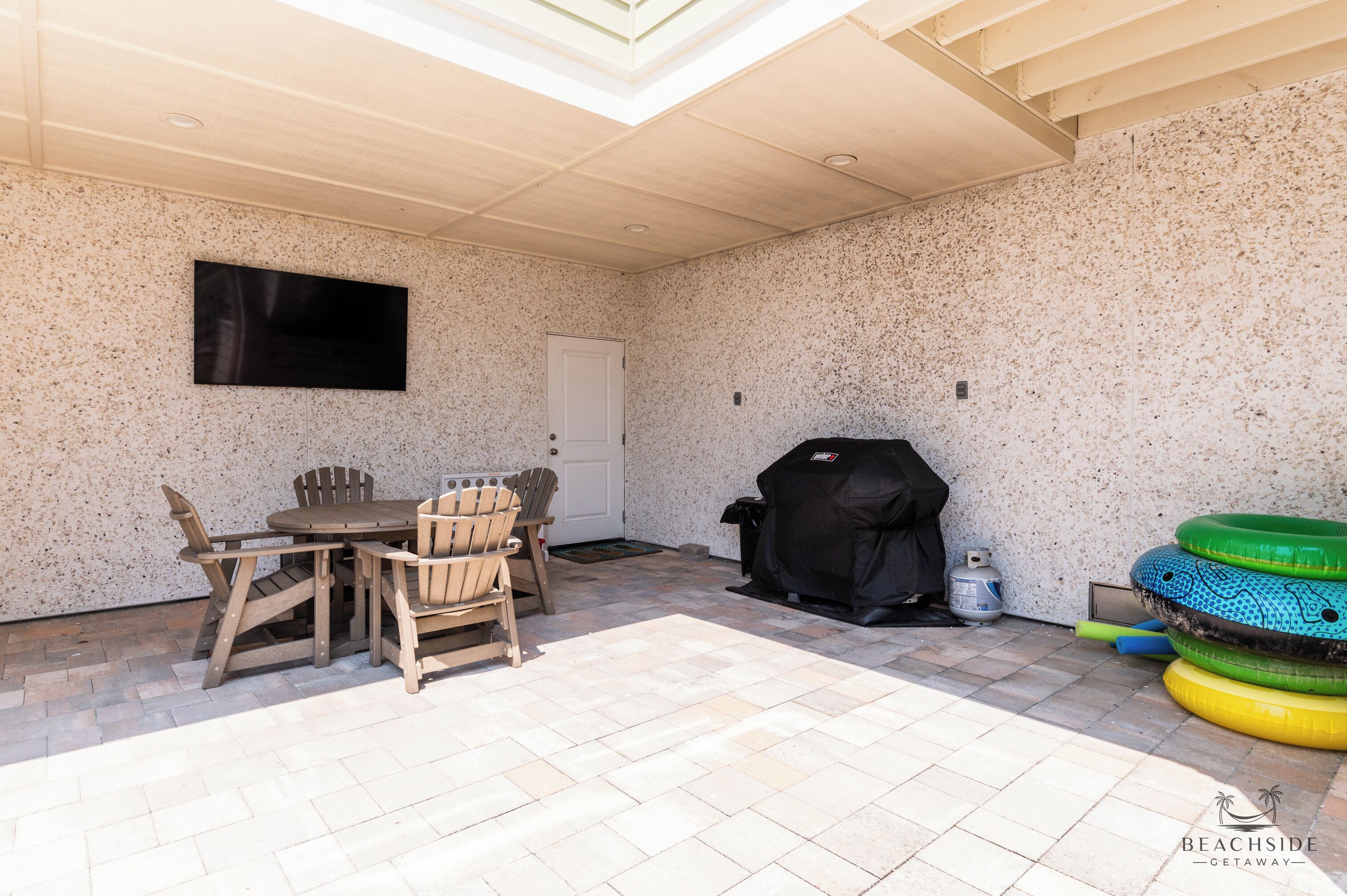 A covered patio with a grill, outdoor seating, and a flat-screen TV.