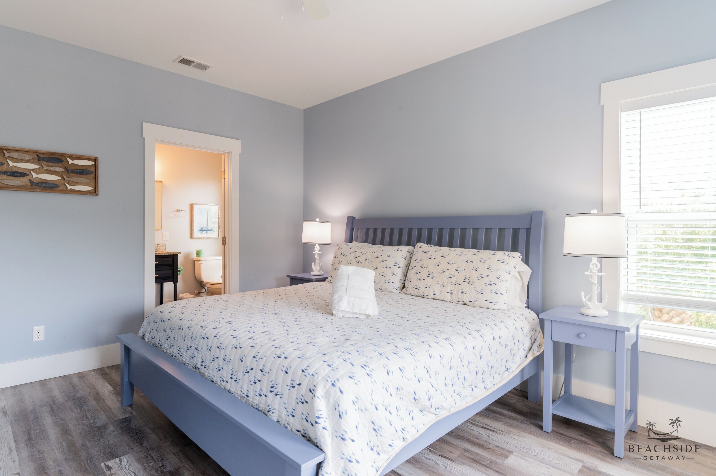 A bedroom with a bed, nightstands, a window with blinds, and a door leading to another room.