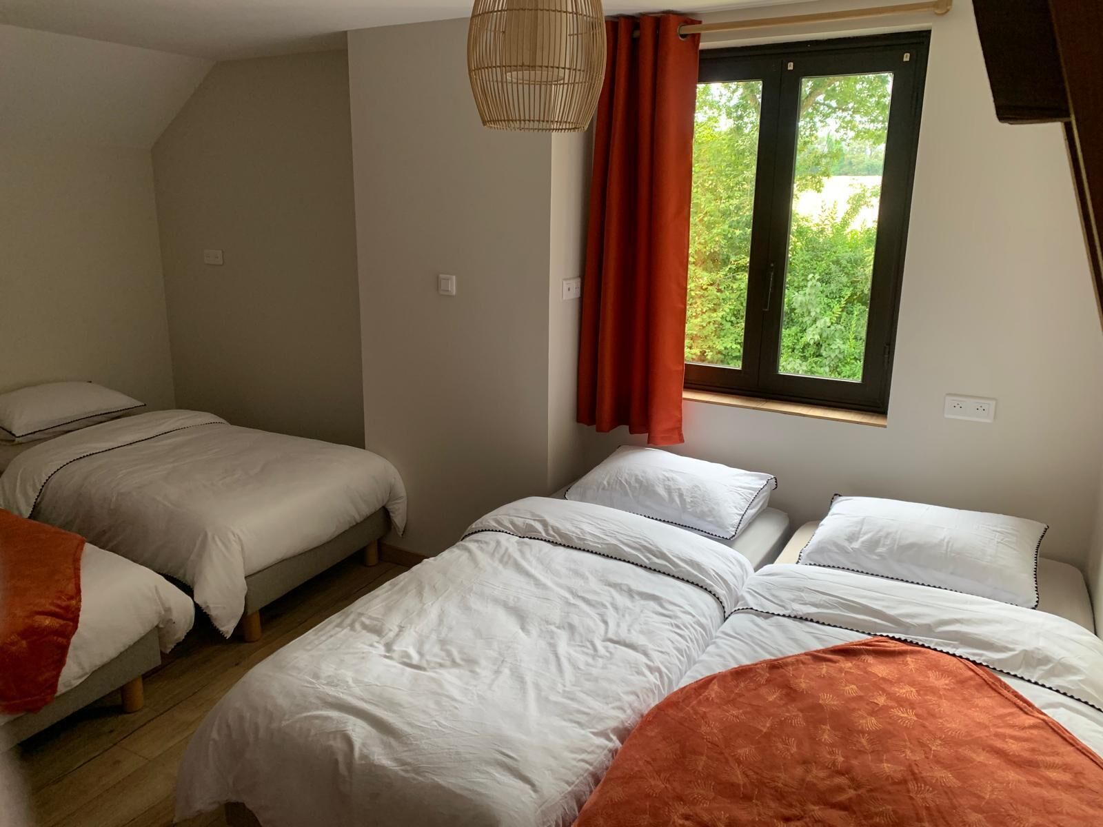Quarto com duas camas de solteiro e uma cama maior, janela com cortinas e luminária suspensa.