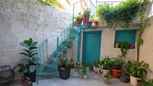 Une cour étroite avec un escalier, des plantes en pot et une petite statue.