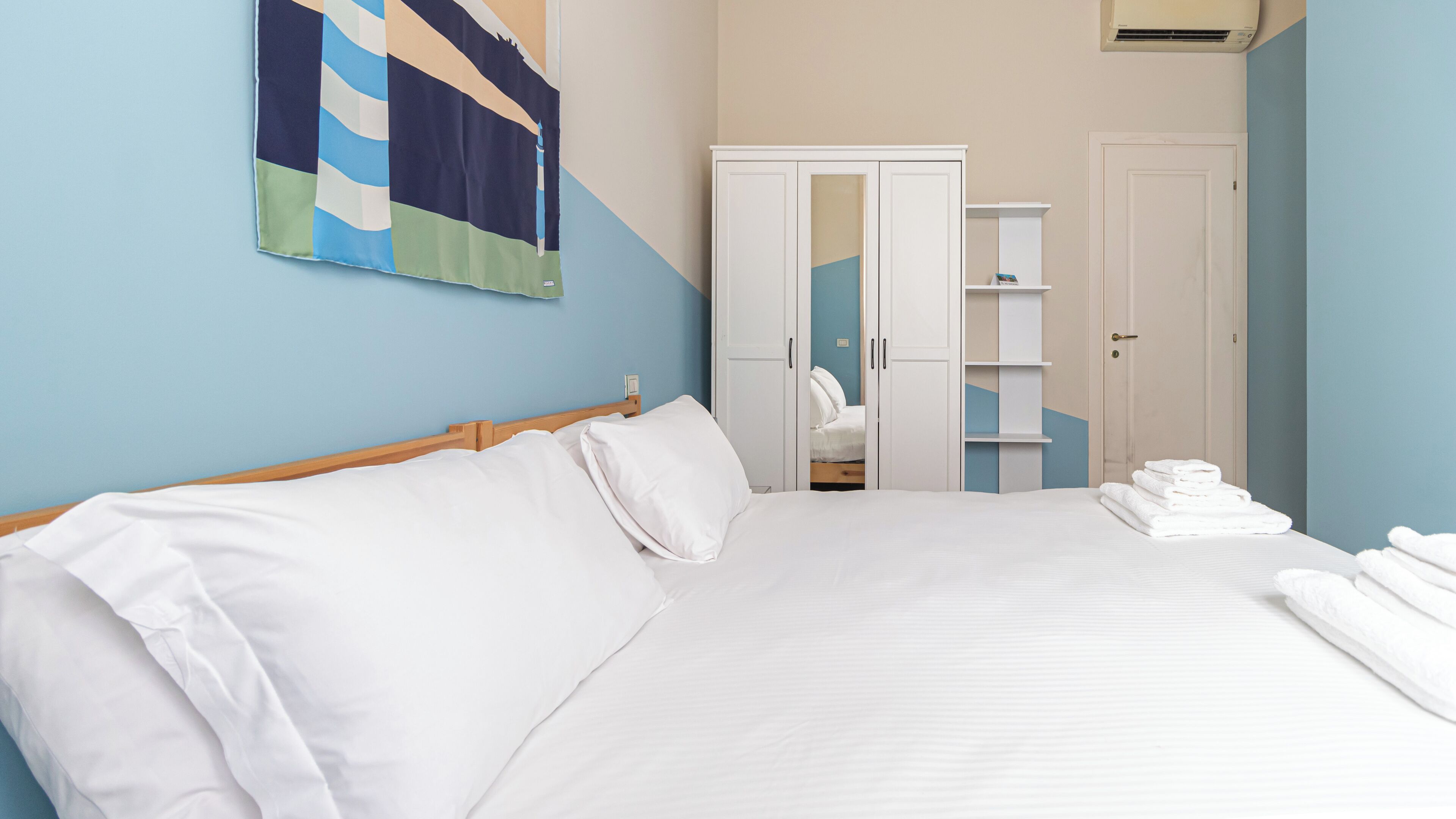 A hotel room with a large bed, a wardrobe, a mirror, and a towel rack.