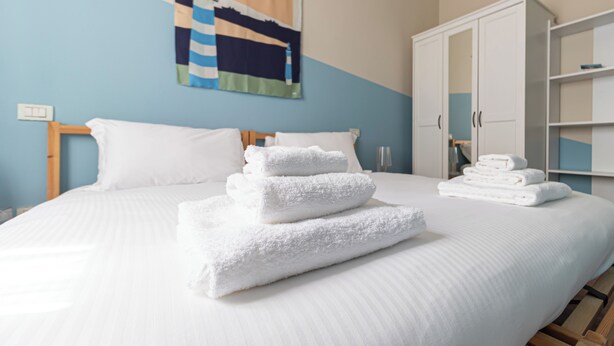 Una cama bien hecha con sábanas y toallas blancas, cabecera de madera, pared de acento azul y armario blanco.