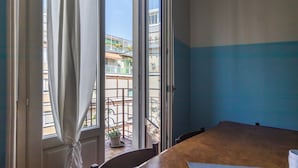 Una habitación con un ventanal grande, vistas a un balcón con planta en maceta y una mesa de madera.