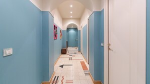 Un pasillo con paredes azules, suelo de baldosas con flechas direccionales, una puerta a la derecha y un pequeño banco en el centro.
