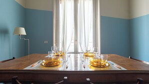 Mesa de comedor con platos, vasos y cubiertos, ubicada frente a una ventana con cortinas.