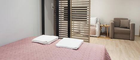 A hotel room with a bed, a chair, a small table, and a sliding door.