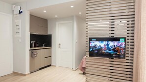 A modern kitchen with a built-in TV, wooden blinds, and a white door. - Petralona Gem Hotel-Style Studio Balcony (Athens)