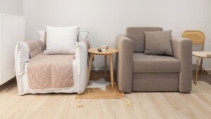 A modern living room with a beige sofa, a matching armchair, and a small round table with a remote control. - Petralona Gem Hotel-Style Studio Balcony (Athens)