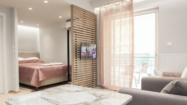 A modern hotel room with a bed, a TV mounted on a wooden panel, a balcony with a view, and a marble table. - Petralona Gem Hotel-Style Studio Balcony (Athens)