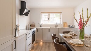 Une cuisine moderne avec des armoires blanches, un four encastré et un coin repas doté d’une table en bois, mise pour quatre personnes.