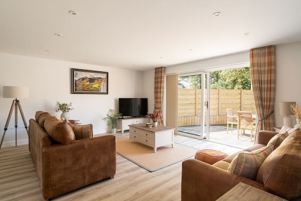 A living room with a sofa, a coffee table, a TV, and a balcony with a table and chairs.