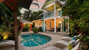 Une maison à deux étages dotée d’une piscine, d’un espace extérieur aménagé et d’une végétation tropicale luxuriante.