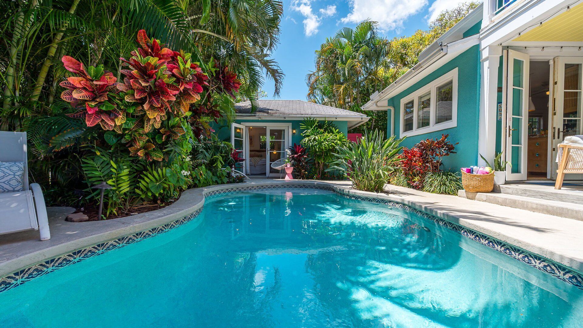 Una piscina rodeada de exuberante vegetación tropical y una casa con fachada luminosa.