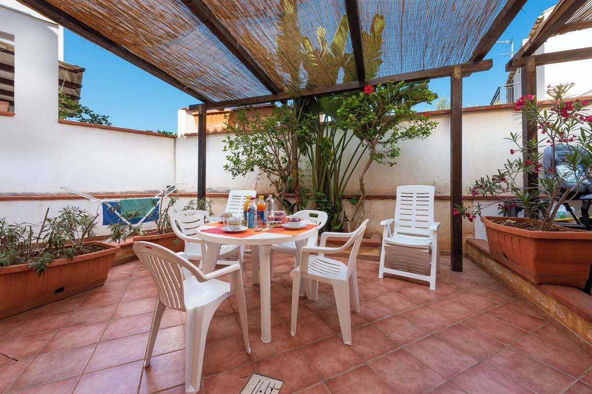 Eine Terrassengruppe mit Tisch und Stühlen, umgeben von Kübelpflanzen und einem Pergola.