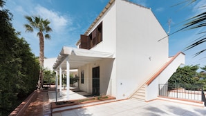 Un edificio blanco con un porche cubierto, una escalera y un patio amurallado.