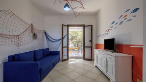 Una habitación con un sofá azul, un armario blanco con televisor y una hamaca.