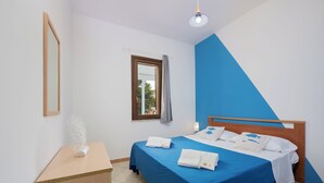 Un dormitorio con cama, mesita de noche, espejo y ventana con cortinas.