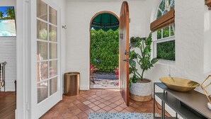 A hallway with a white door, a potted plant, a large bowl, and a window with a view of greenery. - Casa Mía - Palm Beach Boho Escape (West Palm Beach)