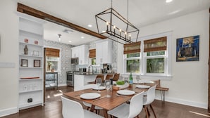 A modern kitchen with white cabinets, a wooden dining table set for six, and a hanging light fixture. - Casa Mía - Palm Beach Boho Escape (West Palm Beach)