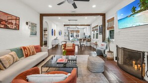 A spacious living area with a fireplace, a ceiling fan, and a dining area in the background. - Casa Mía - Palm Beach Boho Escape (West Palm Beach)