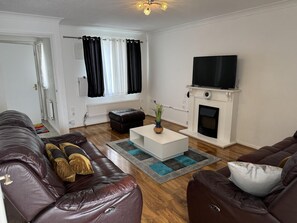 A living room with a brown leather sofa, a white coffee table, a fireplace, and a flat-screen TV. - Luxury London Apartment With 3 Bedrooms (London)