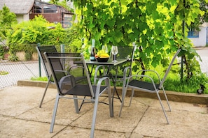 A patio table with chairs, a bottle, and a bowl of fruit.