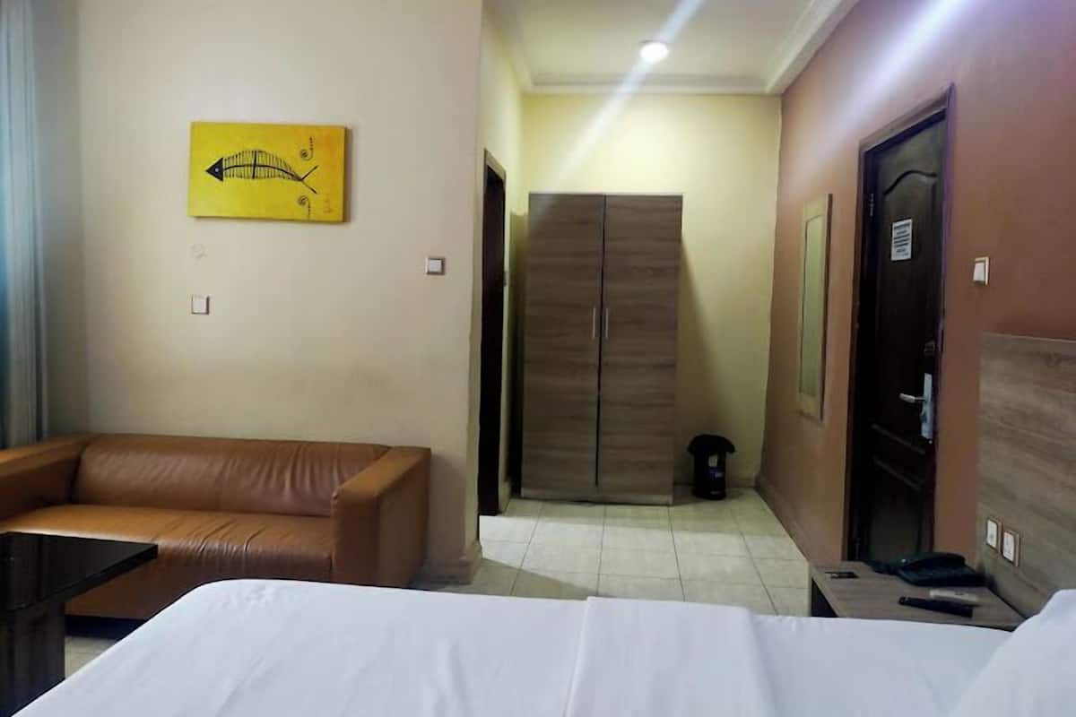 Une chambre d’hôtel avec un lit, un canapé en cuir marron, une armoire en bois et une œuvre d’art jaune accrochée au mur.