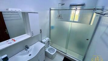 Un baño moderno con cabina de ducha de vidrio, inodoro y lavabo con espejo.