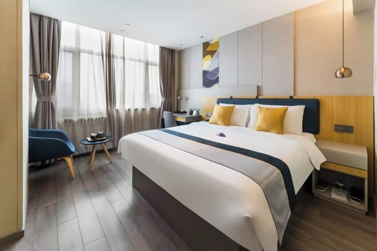 A hotel room with a large bed, a desk, a chair, and a small table.