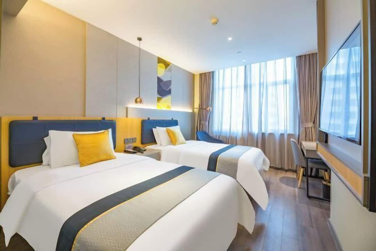 A hotel room with two beds, a desk, a chair, and a large window with curtains.