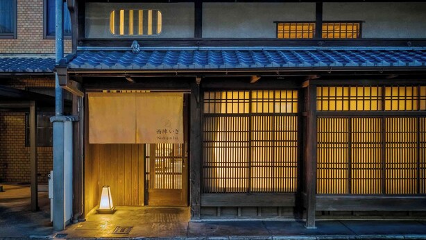 Perinteinen japanilainen rakennus, jossa on puinen julkisivu, suuret liukuvat ovet ja pieni, valaistu lyhty sisäänkäynnin kohdalla.