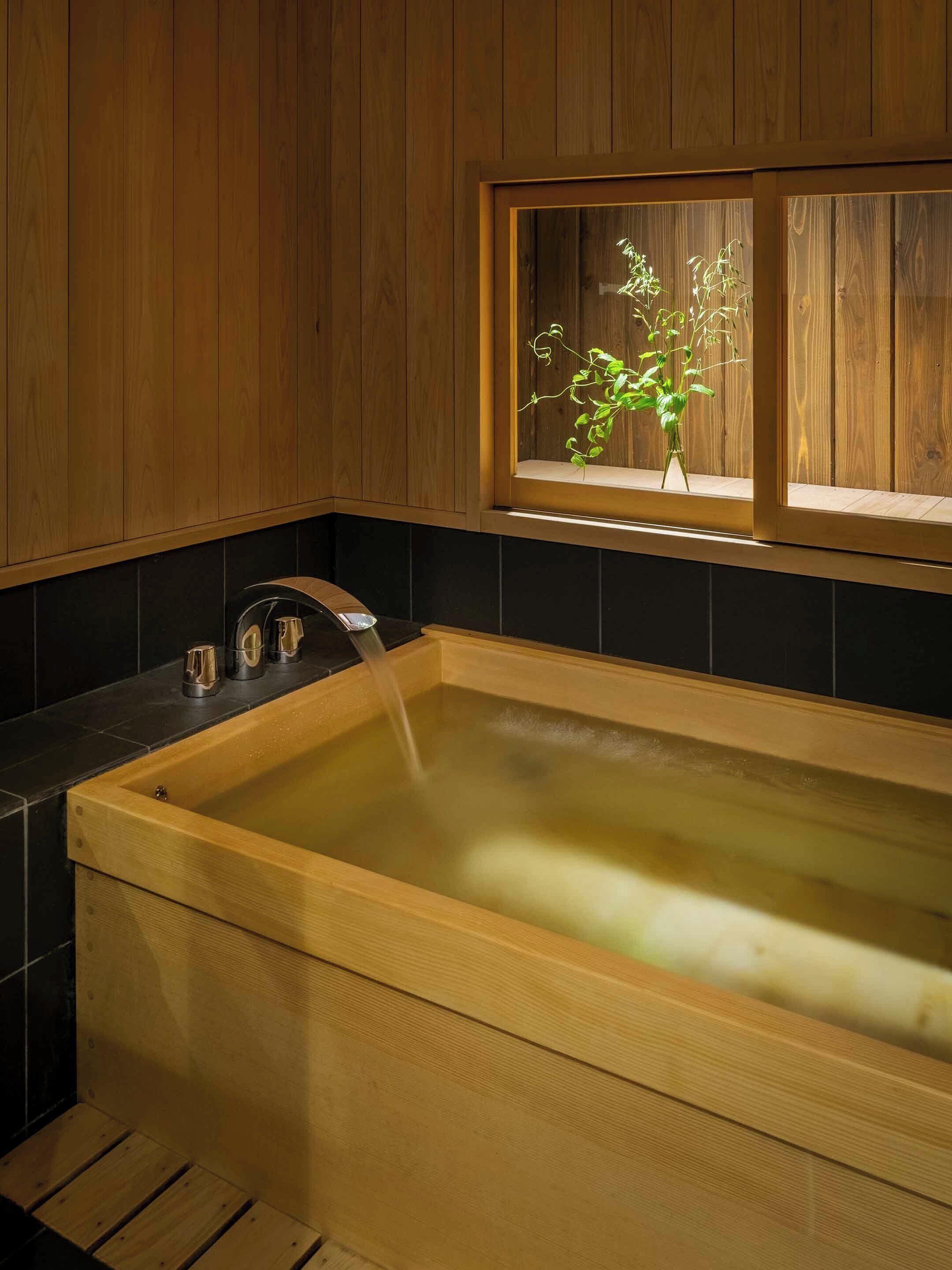 A wooden bathtub with a window above it, a faucet, and a plant inside the window.