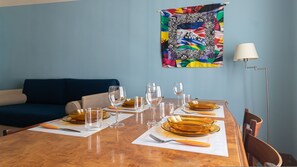 A dining table set with plates, glasses, and cutlery, a sofa, a lamp, and a colorful tapestry on the wall. - Italianway Comfort - Gessi 49 (Milan)