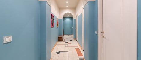 Um corredor com paredes azuis, chão de azulejos com setas indicativas e uma porta no final.
