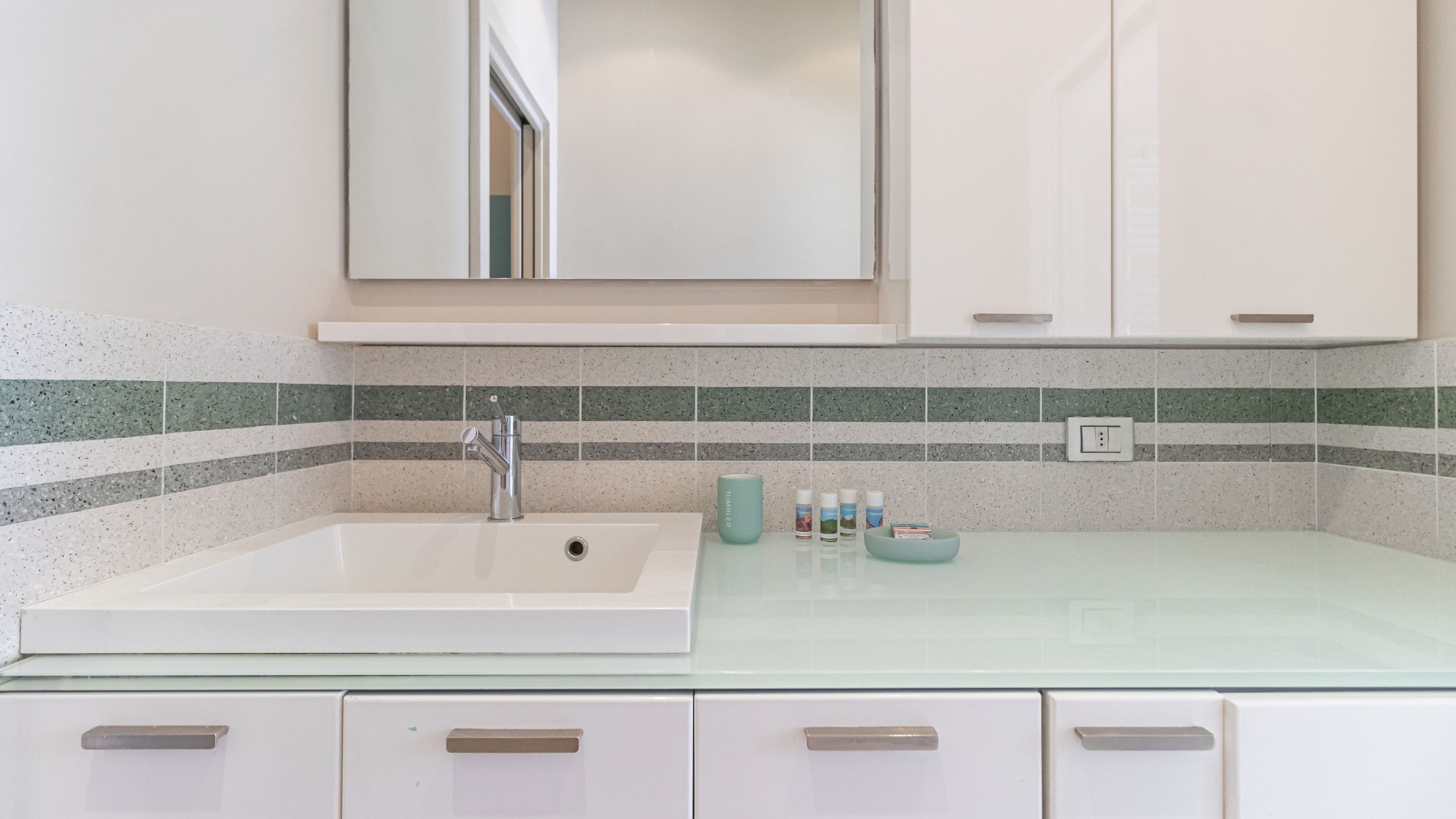 A bathroom with a white sink, a mirror, and a tiled backsplash.
