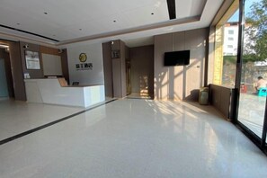 A hotel reception area with a reception desk, a mounted television, and a large window offering a view of the outside. - Liwang Hotel (Libo)