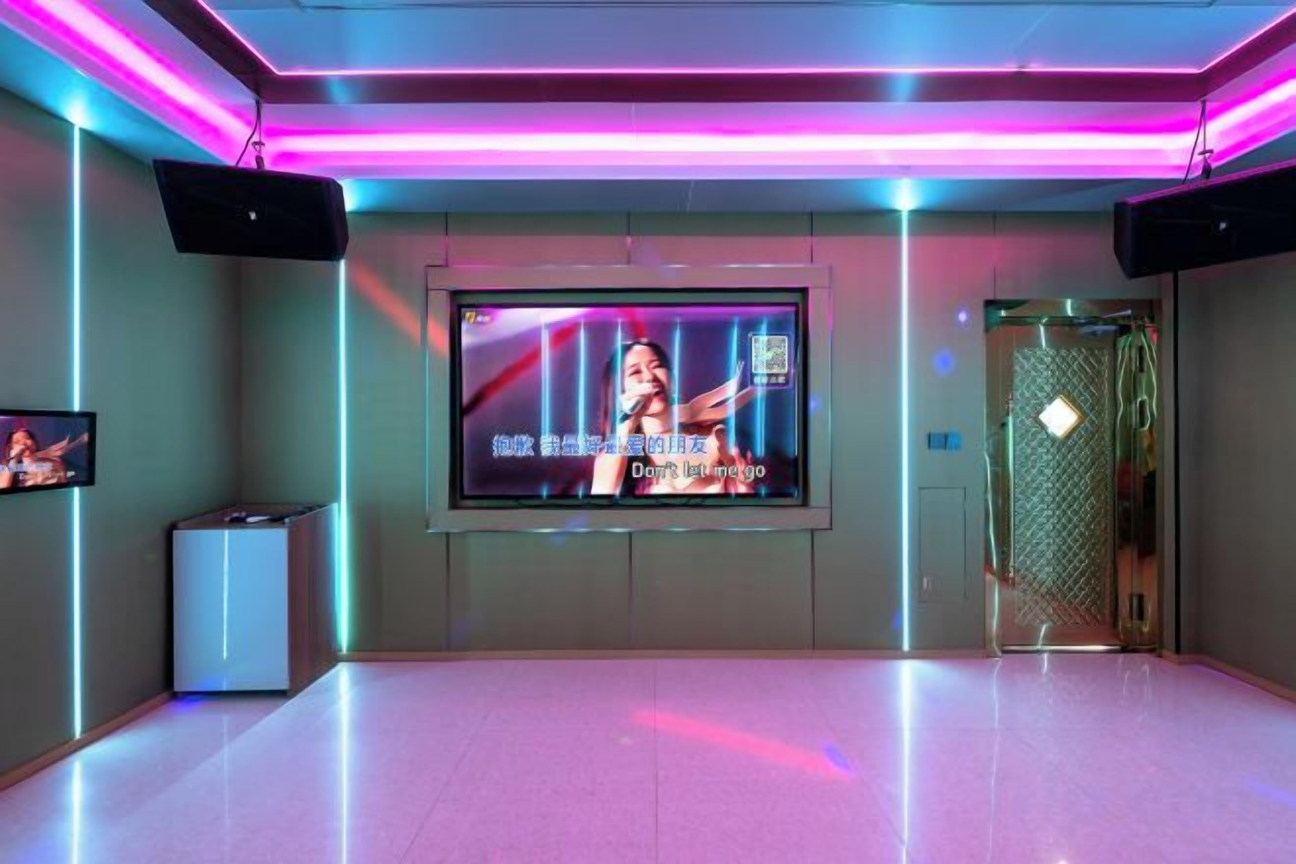 Una habitación moderna con un televisor de pantalla plana grande montado en la pared, un altavoz y una puerta con picaporte metálico.