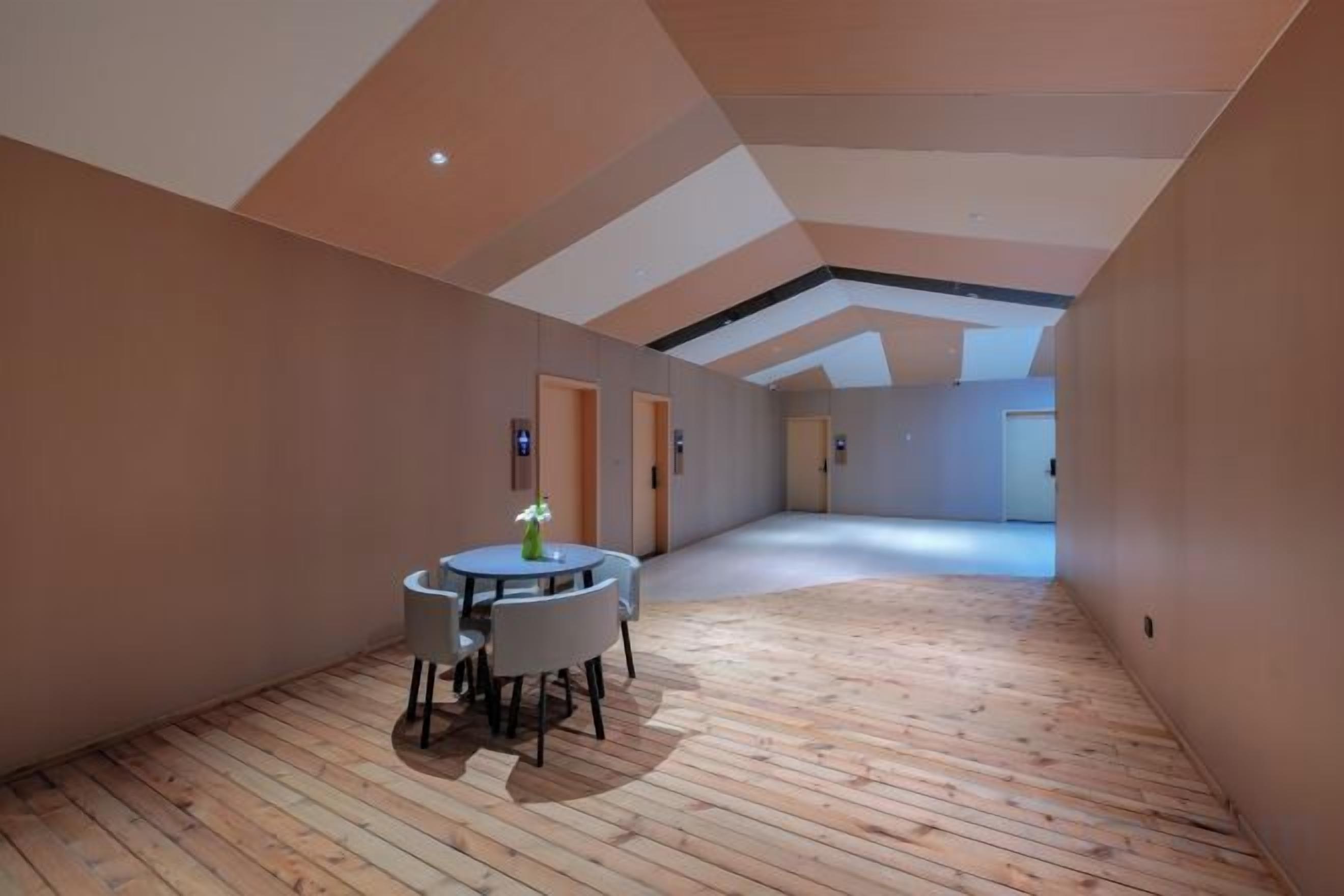 A spacious room with a wooden floor, a round table with chairs, and a door in the background.