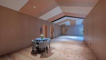 A spacious room with a wooden floor, a round table with chairs, and a door in the background.